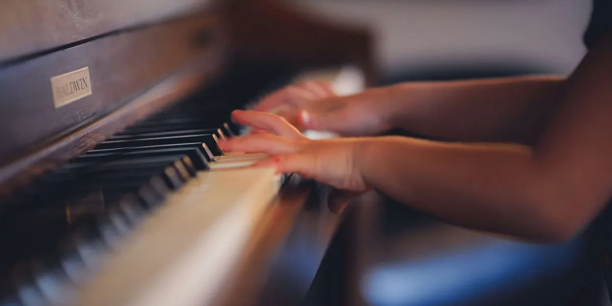 A child's hands playing an upright piano