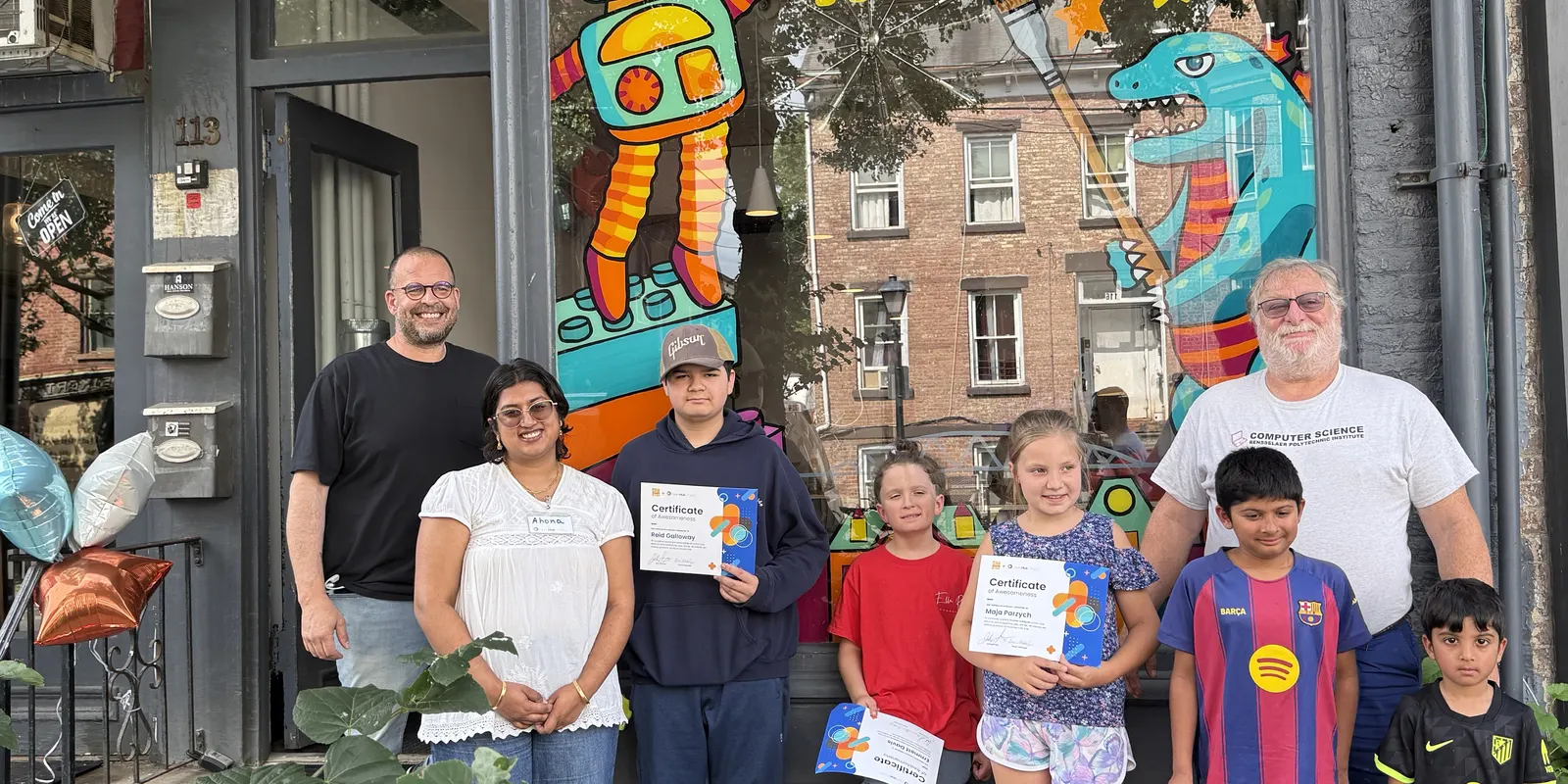 Campers and instructors with their certificates in front of the studio mural